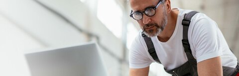 Glasfaserausbau für Unternehmen Ein Handwerker mit Latzhose, der etwas in einen Computer eingibt