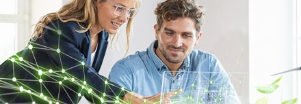 Grün und digital mit EWE business Ein Frau und ein Mann hinter einem Schreibtisch, die eine stilisierte grüne Vernetzung ihres Unternehmens betrachten