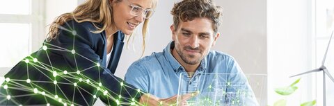Grün und digital mit EWE business Ein Frau und ein Mann hinter einem Schreibtisch, die eine stilisierte grüne Vernetzung ihres Unternehmens betrachten