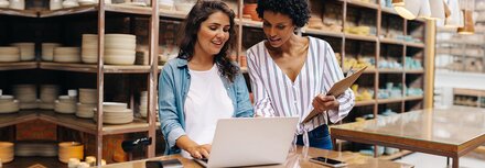Grünes Glasfaser für Ihr Business Zwei junge Ladenbesitzerinnen gucken an der Ladentheke auf ein Notebook und freuen sich