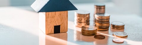 Staatliche Förderung für die Digitalisierung Ihres Unternehmens Ein Haus aus Bauklötzen auf einer Glastischplatte, daneben Münzen
