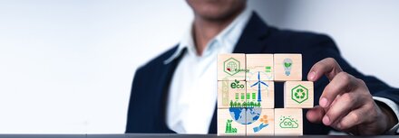 Dekarbonisierung von Unternehmen mit EWE business Ein Mann mit Sakko sortiert mit seiner linken Hand Holzwürfel, die verschiedene Dekarbonisierungsmaßnahmen für Unternehmen darstellen