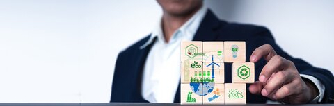 Dekarbonisierung von Unternehmen mit EWE business Ein Mann mit Sakko sortiert mit seiner linken Hand Holzwürfel, die verschiedene Dekarbonisierungsmaßnahmen für Unternehmen darstellen