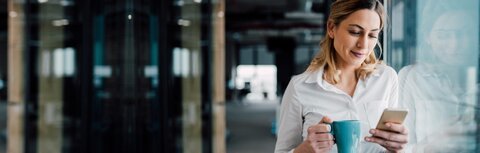 IT-Sicherheit: Was bedeutet was? Eine Frau lehnt an einer Glasfassade und guckt auf ihr Smartphone