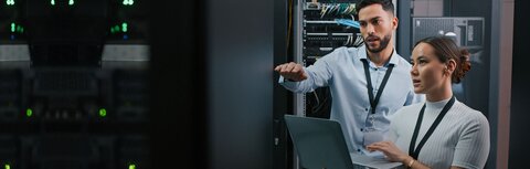 Jetzt vor Zero Day Exploits schützen! Ein Mann und eine Frau mit Laptop, die in einem Serverraum etwas überprüfen