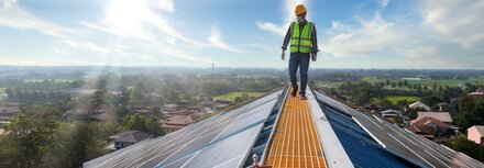 Ratgeber: grüne Energie Ein Wartungstechniker läuft auf einem Fabrikdach, auf dem PV-Module installiert sind
