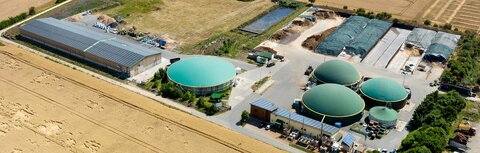 Das Virtuelle Kraftwerk einfach erklärt Eine Luftbildaufnahme einer Biogasanlage, die von landwirtschaftlicher Fläche umgeben ist