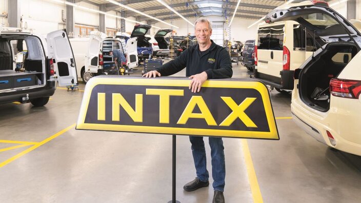Ein Mann mit INTAX-Schild in einer Betriebshalle