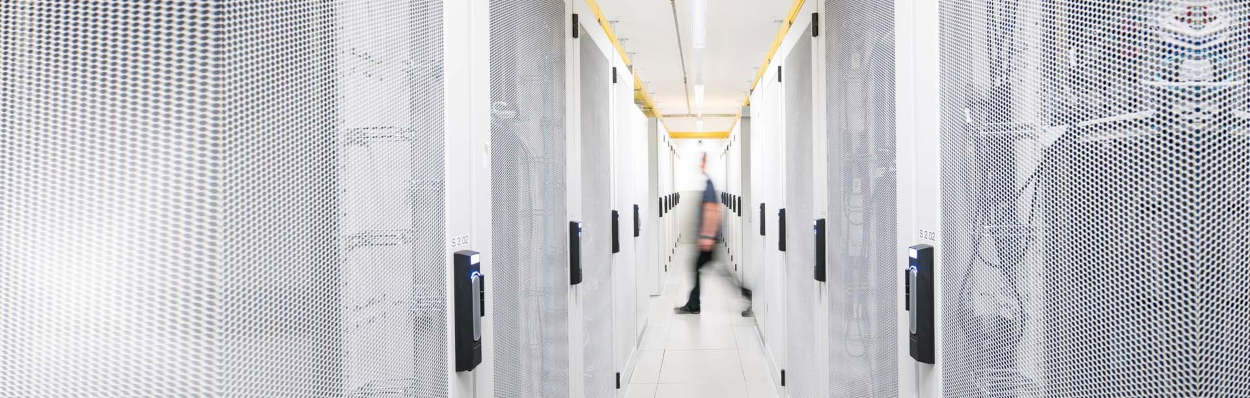 Ein Rechenzentrum mit hellen Server-Racks, im Hintergrund verschwommen eine gehende Person