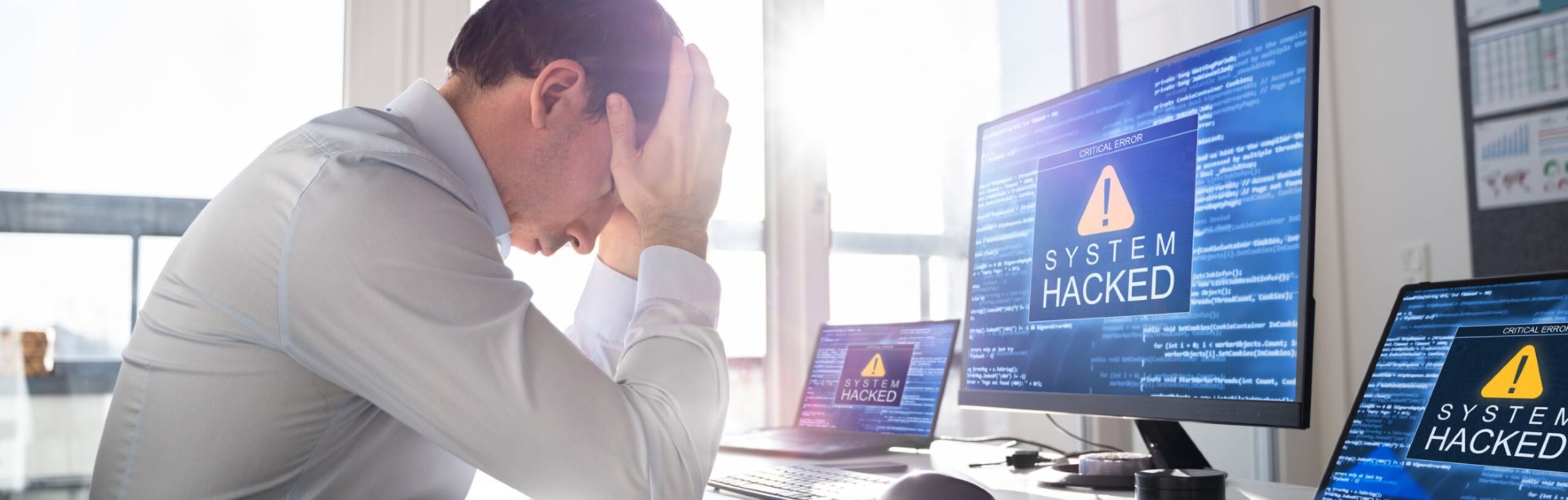 Ein Mann im weißen Hemd schlägt vor dem Rechner, der nach einer Cyberattacke gesperrt wurde, die Hände über dem Kopf zusammen.