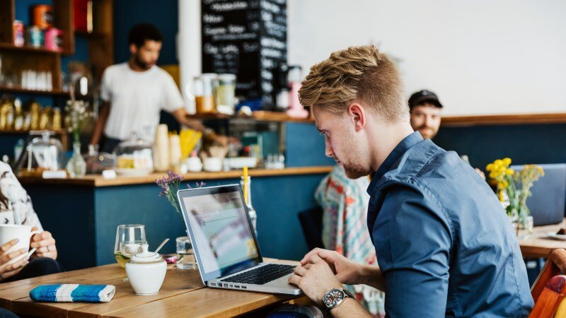 Ein junger Mann arbeitet an seinem Laptop im Cafe