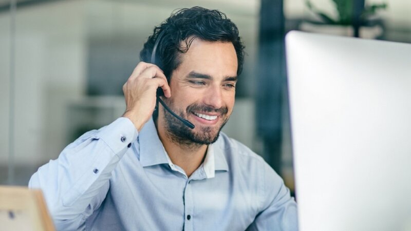 Ein Mann im blauen Hemd sitzt vor einem Computer und arbeitet telefoniert sehr entspannt.