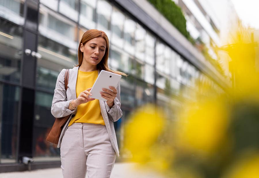 Eine Business-Frau vor einem größeren Gebäude, die etwas auf einem Tablet nachsieht