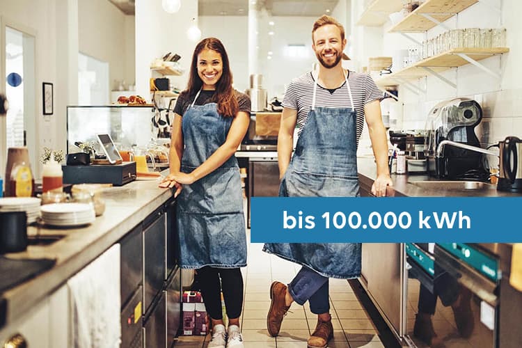 Eine junge Frau und ein junger Mann, die als Baristas in der Küche eines Cafés stehen, darüber ein Hinweis: bis 100.000 kWh