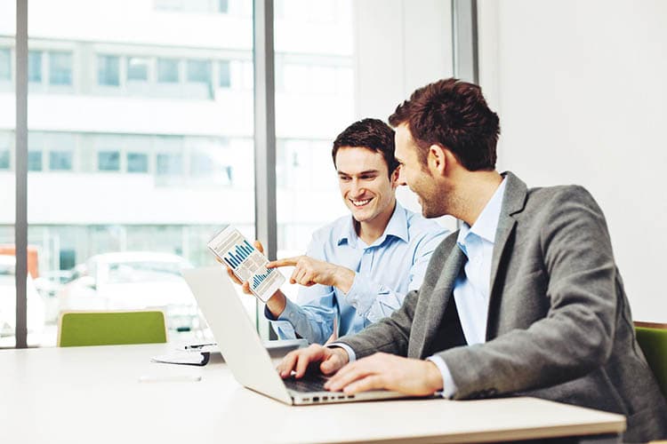 Zwei Männer an einem Arbeitsplatz mit einem Laptop, die ein Diagramm ansehen