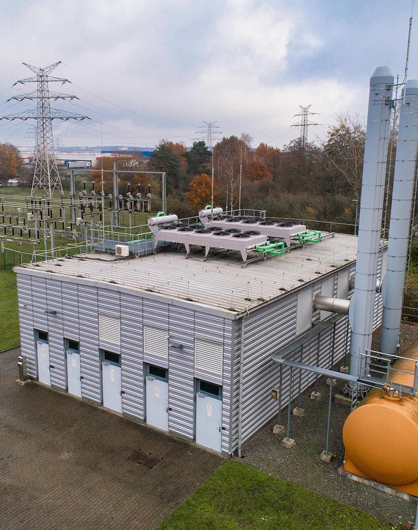 Eine Netzersatzanlage, im Hintergrund Häuser und Strommasten