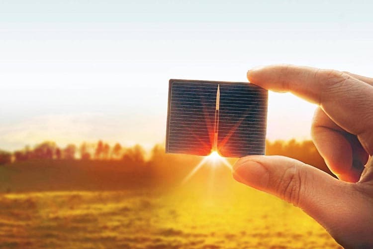 Ein Hand mit PV-Modul vor dem Sonnenuntergang, im Hintergrund eine Wiese
