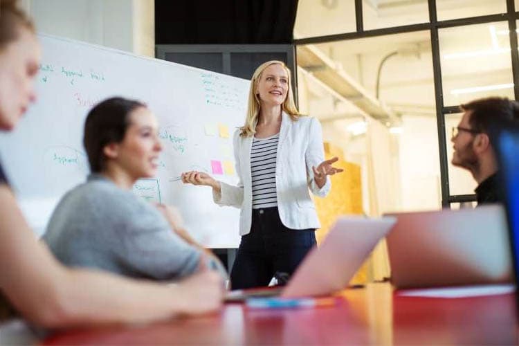 Eine Frau erklärt einer Gruppe etwas an einem Whiteboard.