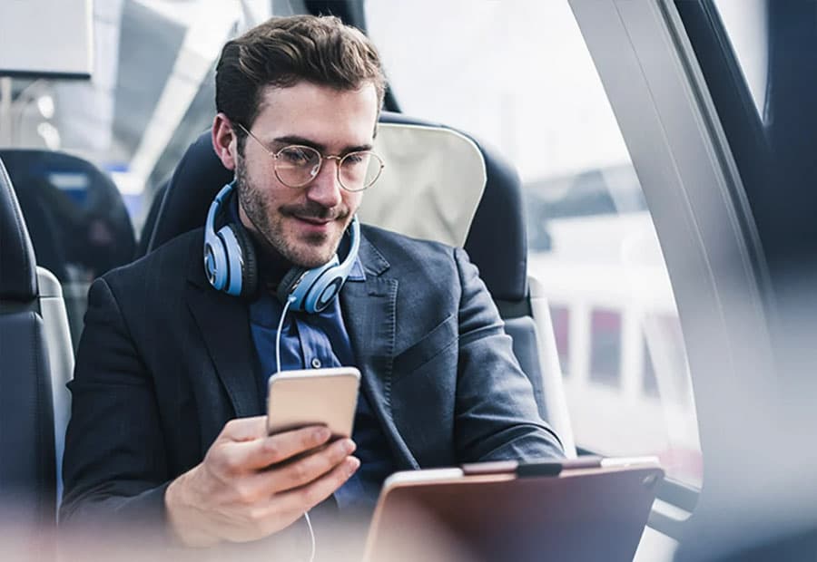 Mann arbeitet im Zug am Laptop mit Smartphone in der Hand.