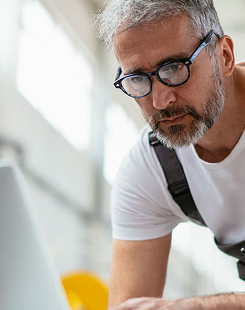 Ein Handwerker mit Latzhose, der etwas in einen Computer eingibt