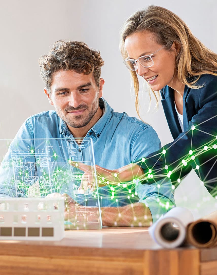 Ein Frau und ein Mann hinter einem Schreibtisch, die eine stilisierte grüne Vernetzung ihres Unternehmens betrachten