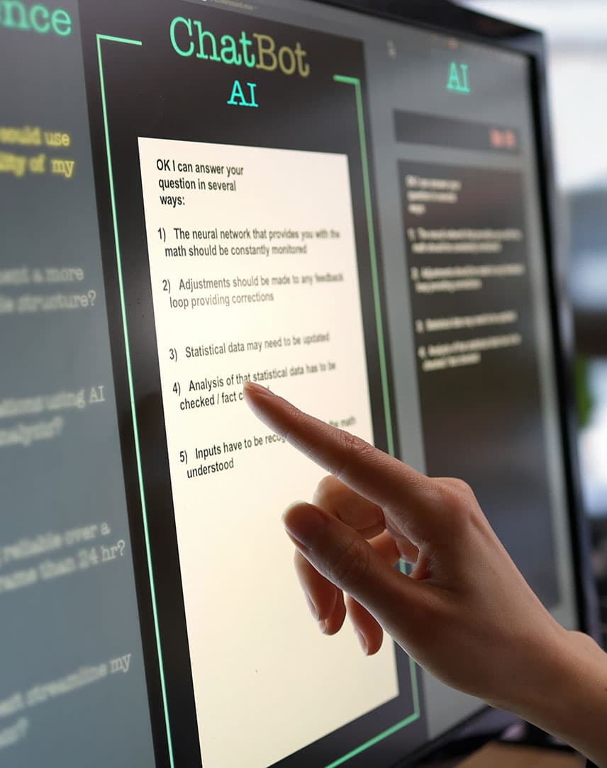 Bildschirme in einem Büro, auf einem wird eine Chatbot-Maske angezeigt.