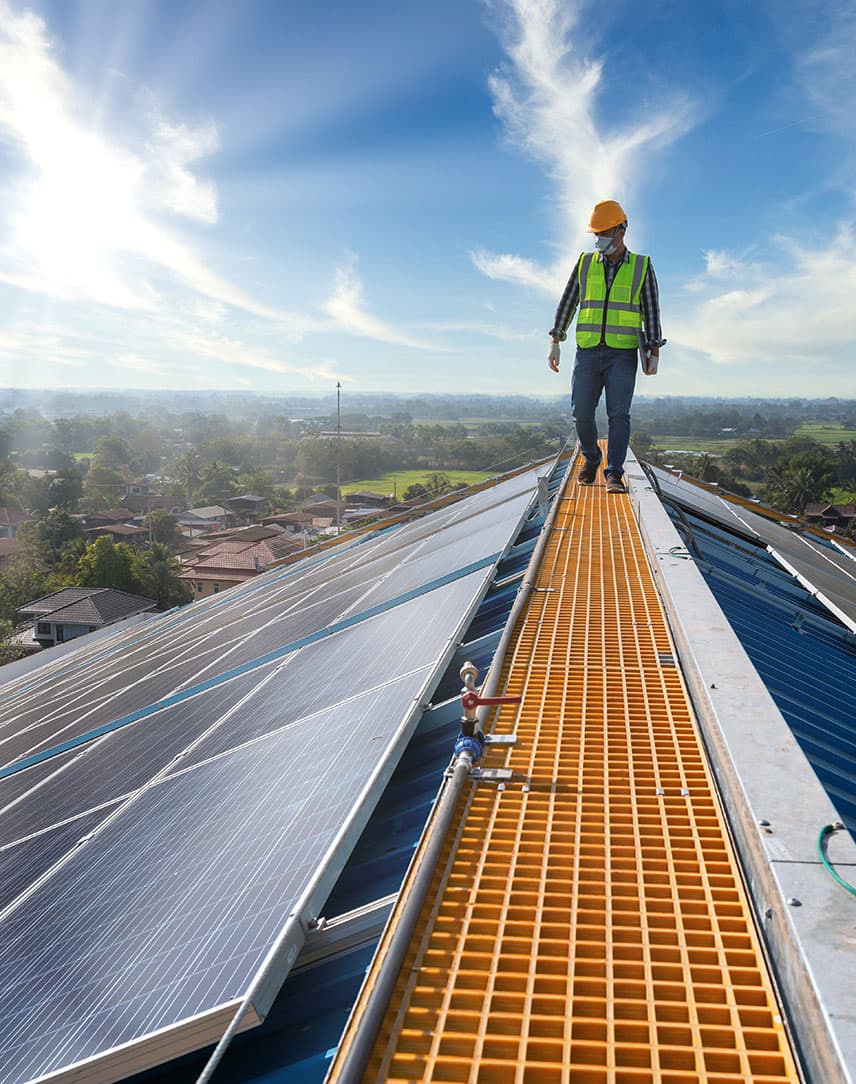 Ein Wartungstechniker läuft auf einem Fabrikdach, auf dem PV-Module installiert sind