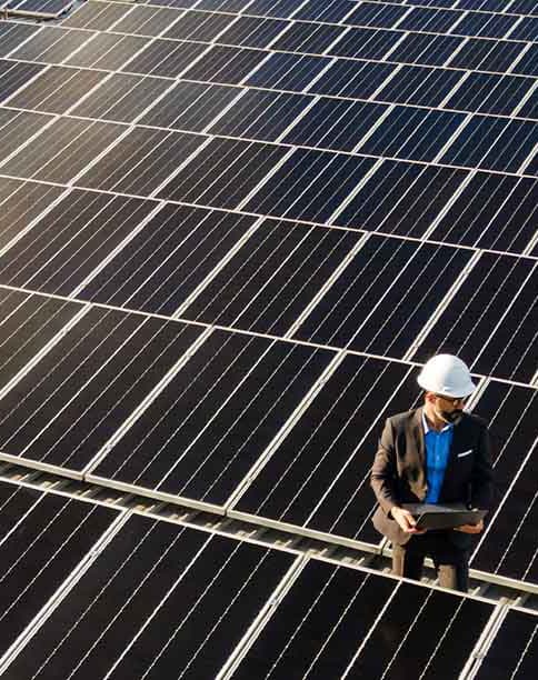 Ein PV-Modul-Feld auf einem Hallendach, darauf ein Mann mit Helm und Meßgerät