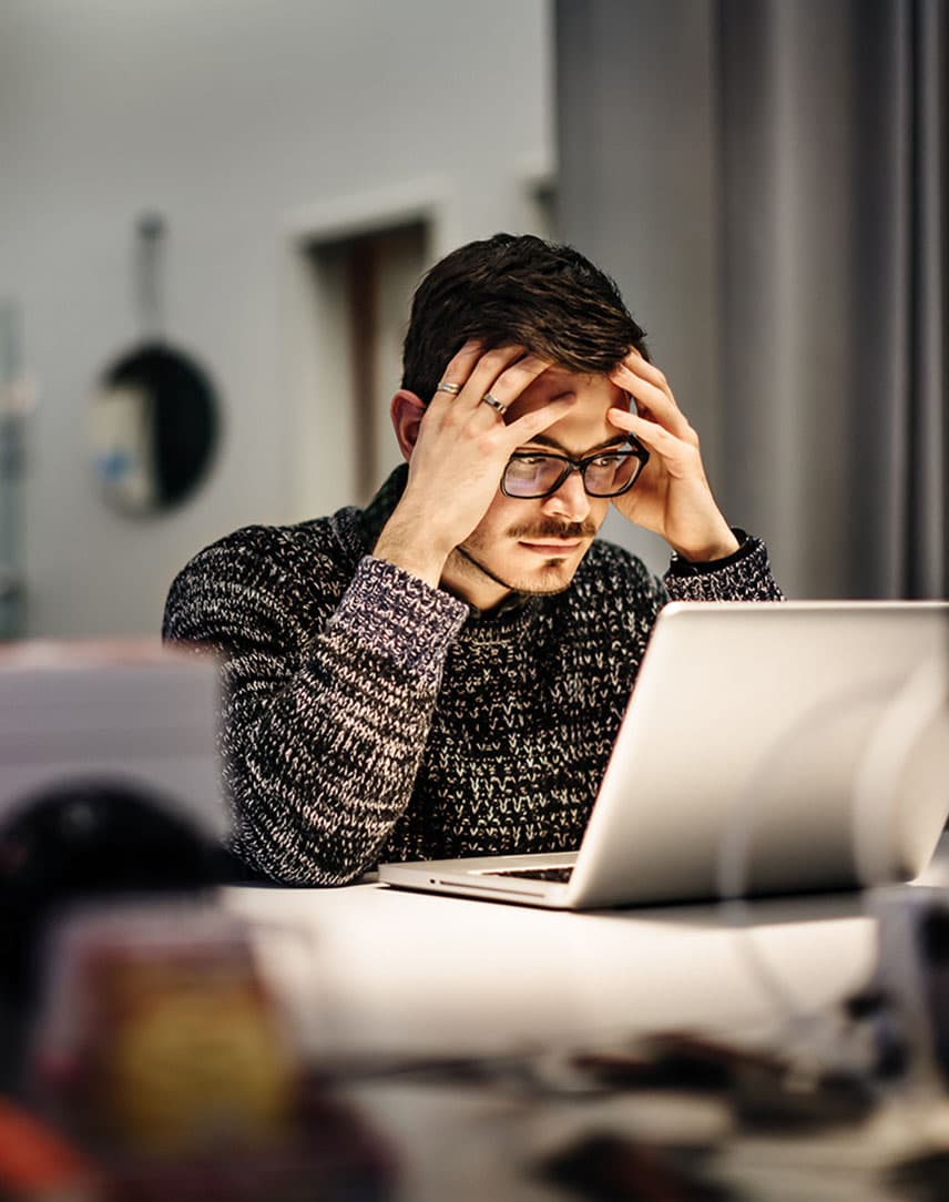Ein Mann sitzt im Büro vor einem Laptop und grübelt über einen erfolgreichen Cyberangriff auf seinen Arbeitgeber nach.