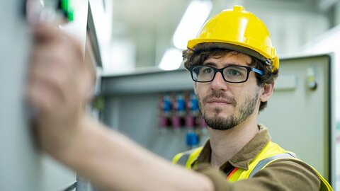 EWE business Wärme für die Pflege: Technik Ein Techniker mit gelbem Helm, der an einer Heizung etwas einstellt