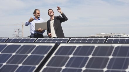 Entwicklung Maßnahmenplan Zwei Männer mit Laptop auf einem Gebäudedach, auf dem Solarmodule installiert sind
