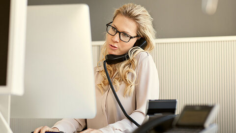 EWE Security Awareness Frau telefoniert am Festnetztelefon und schaut auf Computer-Bildschirm