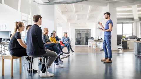 CEO-Fraud Prävention Mann in einem Großraumbüro präsentiert etwas vor einer Gruppe