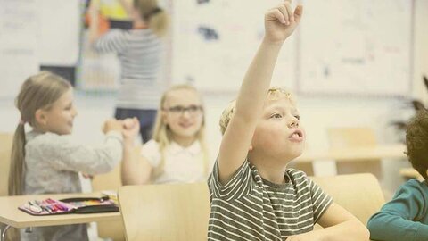 Schule digital Ein Kind meldet sich in einem Klassenraum.