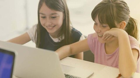 Spielerisches Lernen mit dem Computer Zwei lachende Schulmädchen vor einem Computer