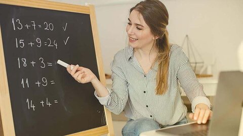 Schule mit Laptop Eine Lehrerin gibt an einer Tafel Matheunterricht, davor ihr Laptop