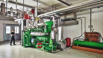 Mit Kraft-Wärme-Kopplung in die Direktvermarktung Ein Blockheizkraftwerk, daneben ein Mann mit Laptop