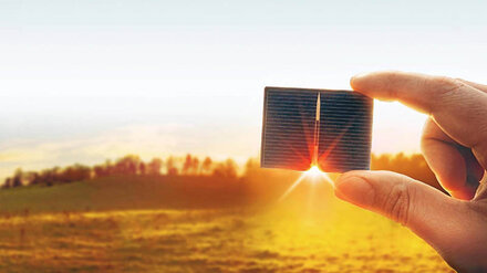 Direktvermarktung für Photovoltaik Ein Hand mit PV-Modul vor dem Sonnenuntergang, im Hintergrund eine Wiese