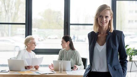 EWE business Erdgas Eine Businessfrau in einem Büro, im Hintergrund zwei weitere Mitarbeiterinnen an einem Bürotisch