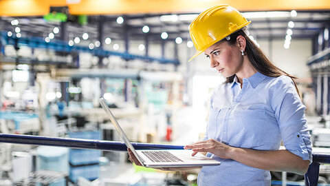 EWE Leased Line Frau mit Helm in Fabrikhalle schaut auf Laptop