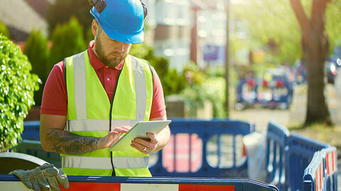 Glasfaserausbau Bauarbeiter mit Weste und Helm draußen am Tablet