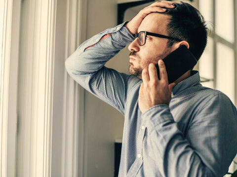 Phishing Mann telefoniert am Handy und fasst sich erschöpft an den Kopf