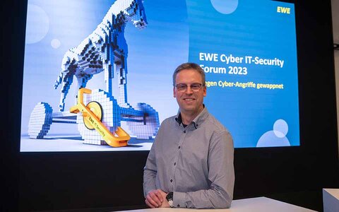 EWE business Referenz Dennis Prior Mann mit Brille vor Präsentationsbildschirm auf Cyber IT-Forum