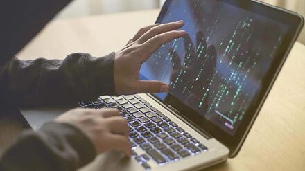 Sicherheit für die digitale Schule Eine Person im dunklen Hoodie bedient einen Laptop, auf dem binäre Zahlenreihen zu sehen sind.